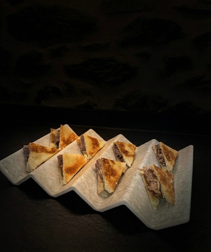 Tostas servidas sobre un soporte ceramico blanco en zigzag, sobre fondo negro