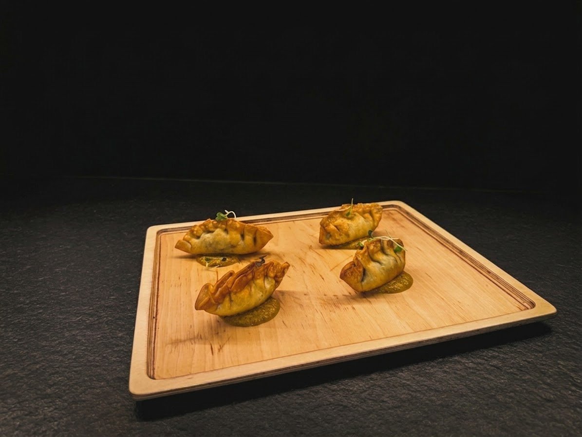 Cuatro empanadillas fritas servidas sobre tabla de madera, sobre fondo negro
