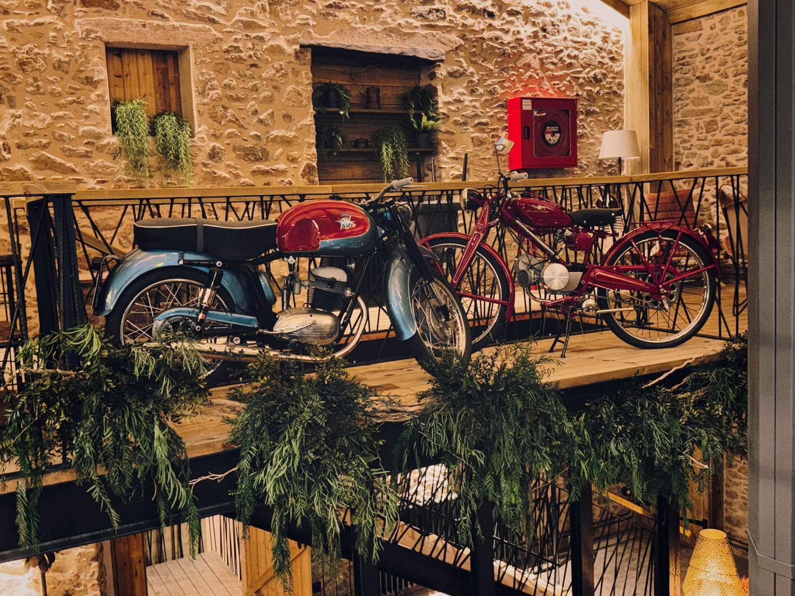 Motos antiguas alineadas en la pasarela de madera, frente al muro de piedra